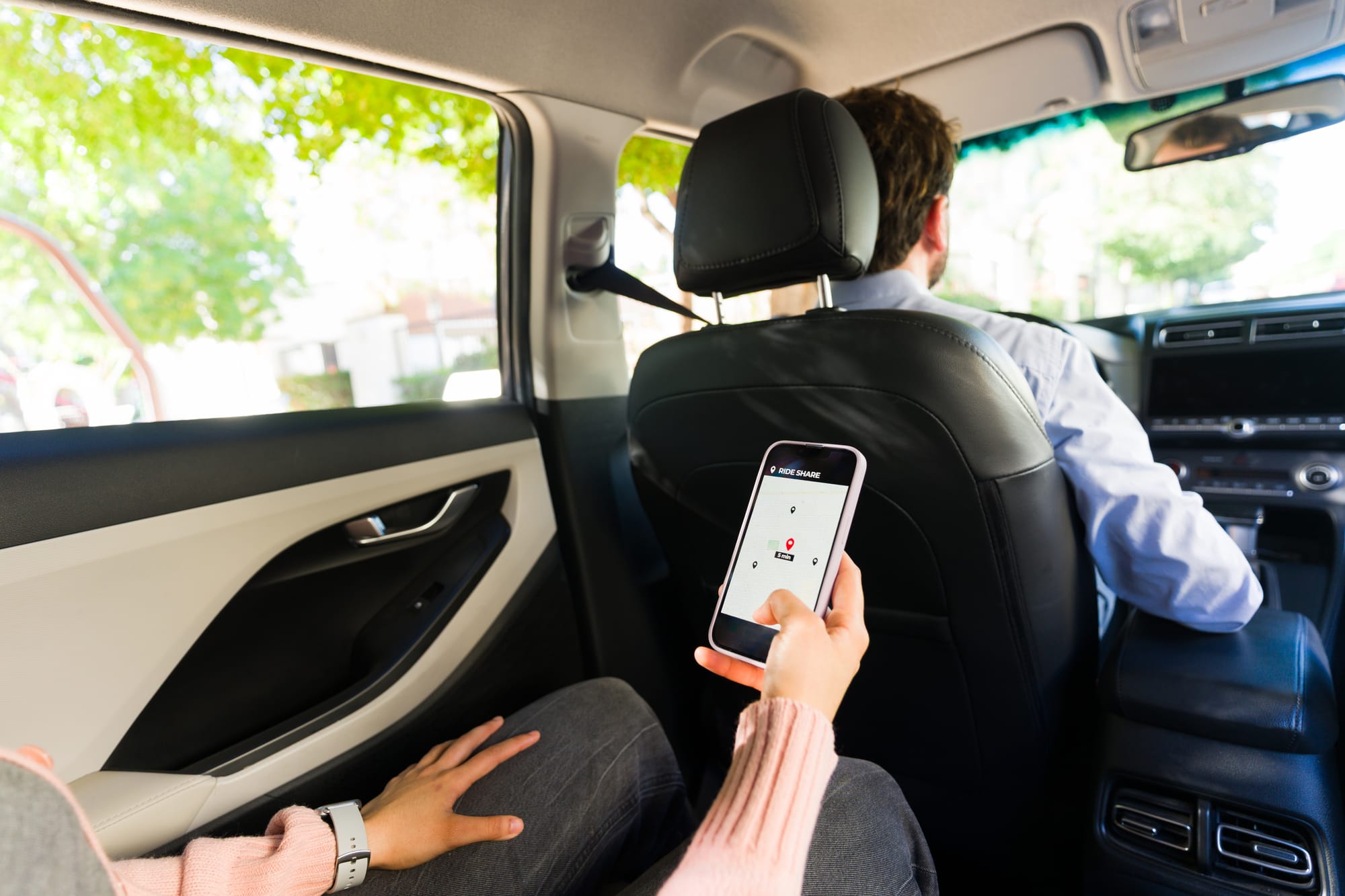 A passenger using a smartphone with a rideshare app, tracking location and navigation while traveling in a car with a male rideshare driver.