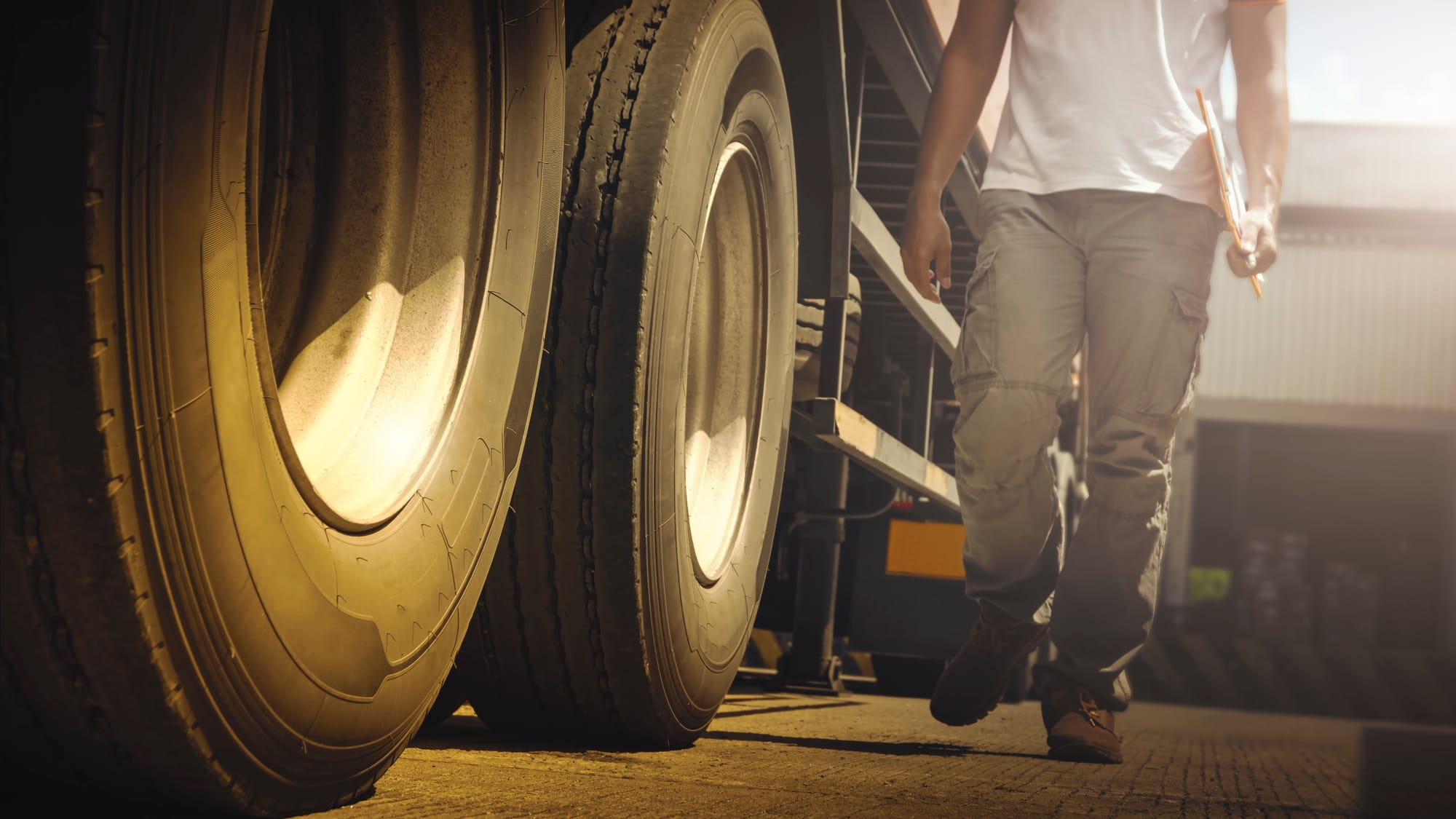 Big semi trailer truck wheels with a man walking next to the vehicle inspecting it for safety issues.