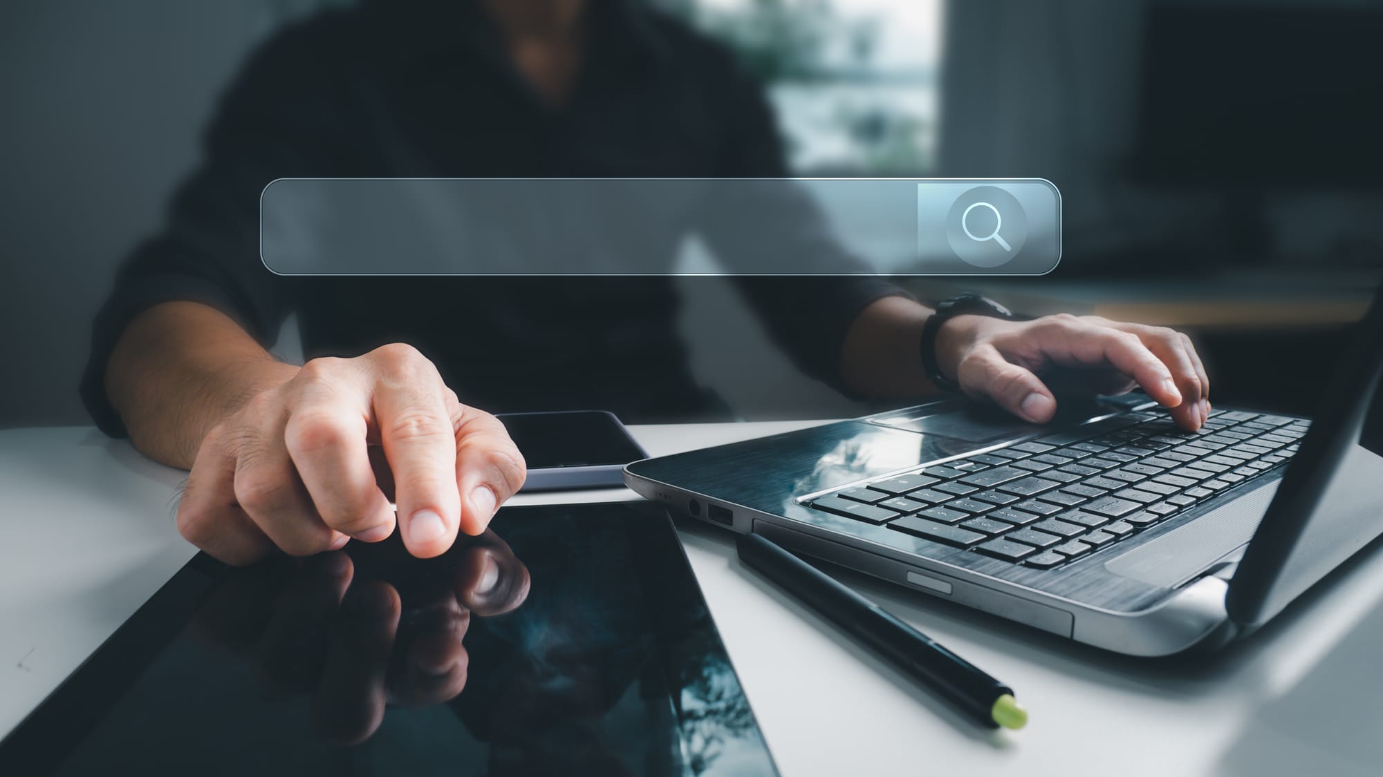 Man working with a tablet, phone and laptop on a desk in the office with Internet search bar.