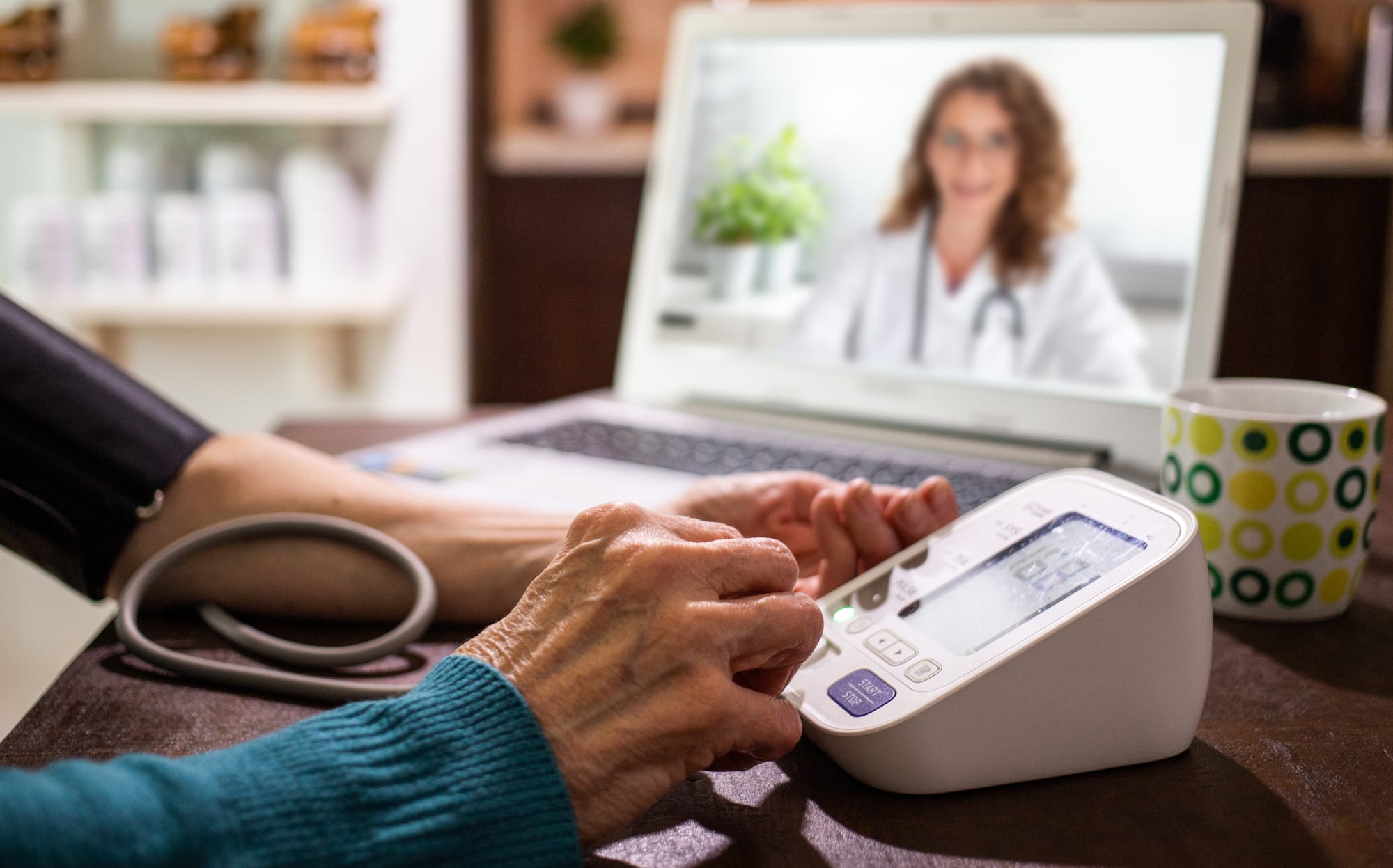 Older patient checking blood pressure during a telehealth visit on their laptop with a female doctors.