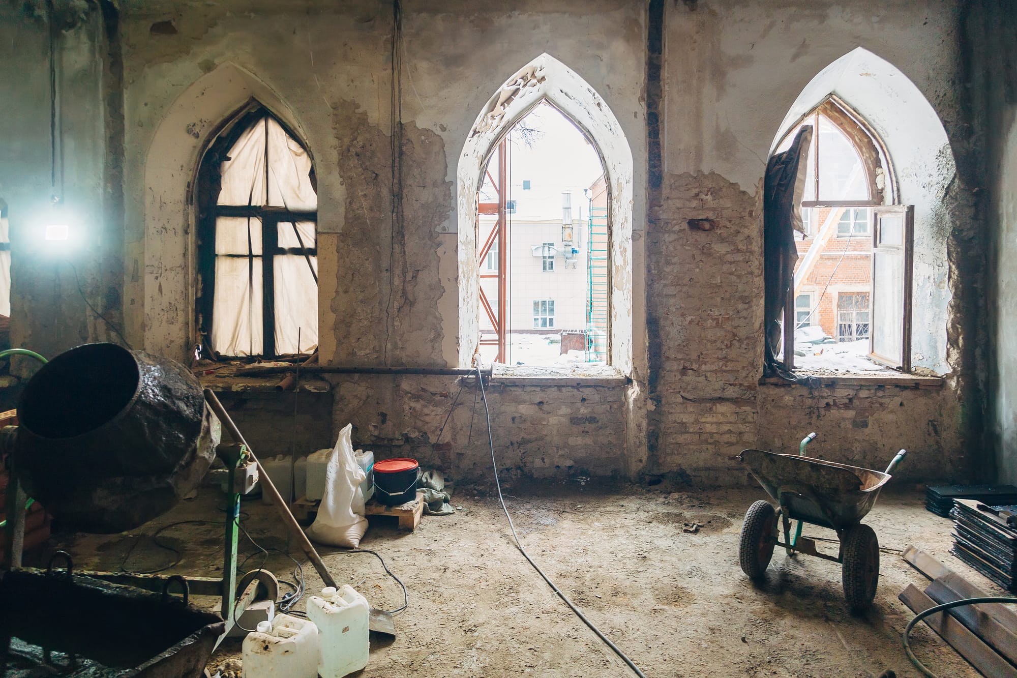 The interior of an old building being renovated. Wheelbarrow and other construction tools are visible.