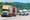 Lots of commerical trucks and other vehicles sharing a highway with green trees and hilly landscape in the background.